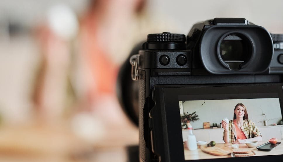 A woman filming a cooking vlog in her kitchen using a digital camera.